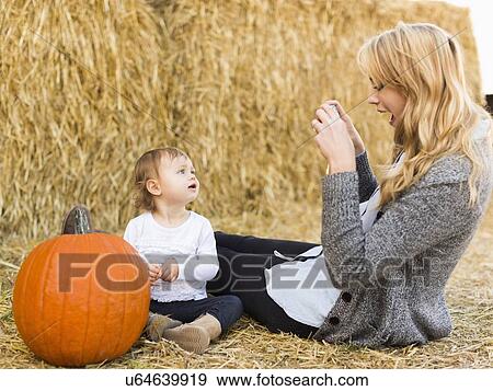 Stock Photo - Mother photographing daughter (12-17 months) with large pumpkin. Fotosearch