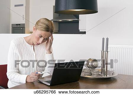 Overworked woman using laptop and holding thermometer View Large Photo Image Stock Photograph - Overworked woman using laptop and holding thermometer. Fotosearch