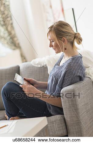 Picture - Pensive woman sitting on sofa with tablet pc. Fotosearch