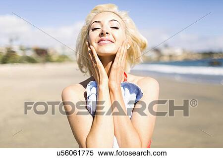 Stock Photography - Portrait of blond woman on beach applying sun screen. Fotosearch