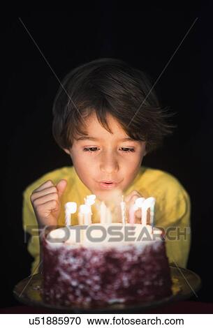 Stock Image - Portrait of boy (6-7) blowing out birthday candles . Fotosearch