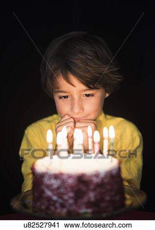 Stock Image - Portrait of boy (6-7) thinking of birthday wishes, Looking at birthday cake. Fotosearch
