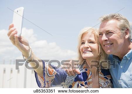 Stock Image - Portrait of couple posing for smartphone selfie. Fotosearch