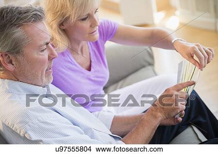 Portrait of couple sitting on sofa looking at sheet of paper View Large Photo Image Picture - Portrait of couple sitting on sofa looking at sheet of paper. Fotosearch