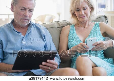 Portrait of couple sitting on sofa using digital tablet and smart phone View Large Photo Image Stock Image - Portrait of couple sitting on sofa using digital tablet and smart phone. Fotosearch
