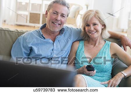 Portrait of couple sitting on sofa watching TV View Large Photo Image Stock Image - Portrait of couple sitting on sofa watching TV. Fotosearch