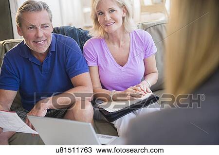 Portrait of couple sitting on sofa smiling at woman in blurred foreground View Large Photo Image Stock Image - Portrait of couple sitting on sofa smiling at woman in blurred foreground. Fotosearch