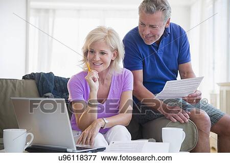 Stock Photo - Portrait of couple sitting on sofa using laptop. Fotosearch