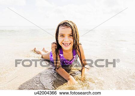 Stock Photograph - Portrait of girl (6-7) lying in sand on beach. Fotosearch