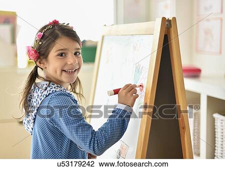 Stock Image - Portrait of girl (6-7) writing on board in classroom. Fotosearch