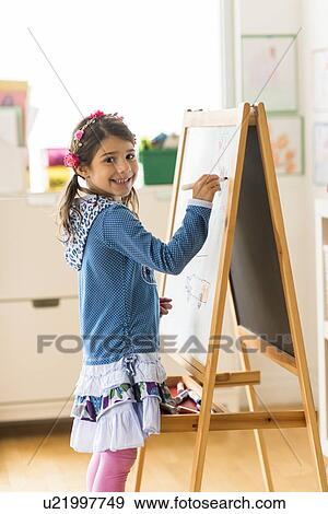 Portrait of girl (6-7) writing on board in classroom View Large Photo Image Stock Photo - Portrait of girl (6-7) writing on board in classroom. Fotosearch