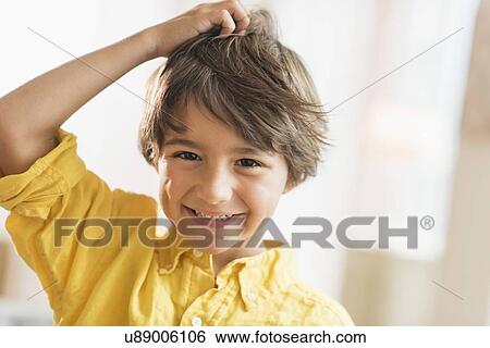 Stock Photograph - Portrait of smiling boy (6-7) with hand in hair. Fotosearch