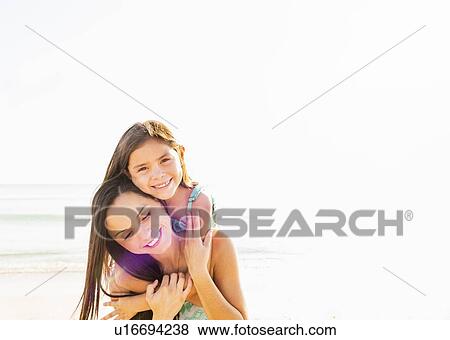Stock Photo - Portrait of smiling girl (6-7) with her mom on beach. Fotosearch
