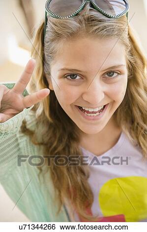 Stock Photograph - Portrait of smiling teenage girl (12-13) showing peace sign. Fotosearch