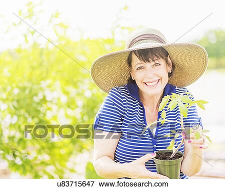 Stock Photo - Portrait of smiling woman holding potted plant in garden. Fotosearch