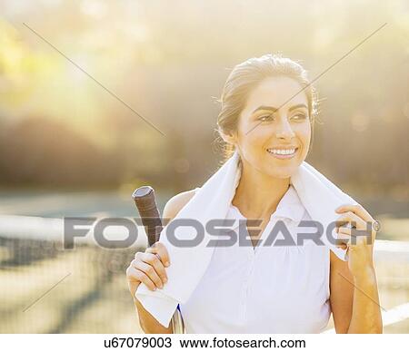 Stock Image - Portrait of smiling young woman with towel and tennis racket . Fotosearch