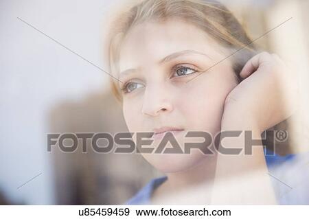 Stock Photo - Portrait of teenage girl (12-13) looking through window. Fotosearch
