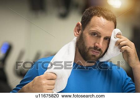 Stock Image - Portrait of tired man wiping face with towel. Fotosearch