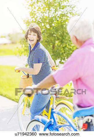 Stock Image - Portrait of woman looking over shoulder at senior man, while getting on bicycle and laughing. Fotosearch