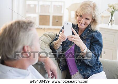 Portrait of woman photographing man with smartphone, sitting on sofa View Large Photo Image Stock Photo - Portrait of woman photographing man with smartphone, sitting on sofa. Fotosearch