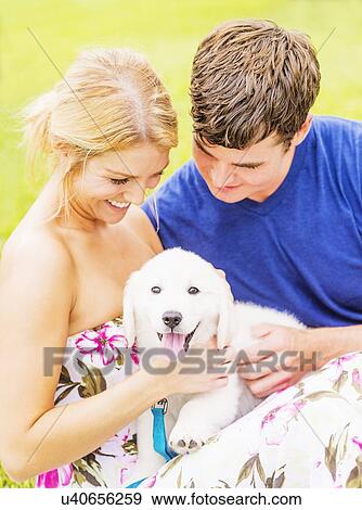 Stock Photo - Portrait of young couple caressing white puppy. Fotosearch