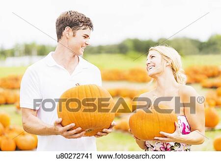 Stock Image - Portrait of young couple holding pumpkins. Fotosearch