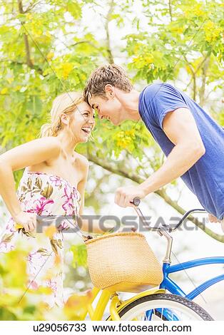 Portrait of young couple sitting on bicycles, touching foreheads, laughing View Large Photo Image Stock Image - Portrait of young couple sitting on bicycles, touching foreheads, laughing . Fotosearch