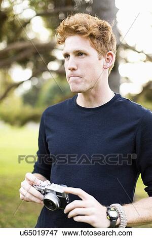 Stock Photo - Portrait of young man holding camera. Fotosearch