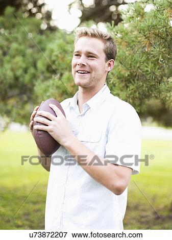 Portrait of young man holding football in park View Large Photo Image Stock Photo - Portrait of young man holding football in park. Fotosearch