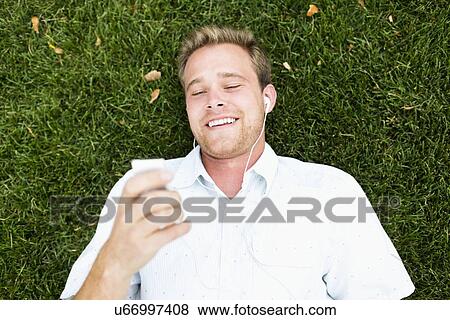 Portrait of young man listening to music in park View Large Photo Image Stock Photo - Portrait of young man listening to music in park. Fotosearch