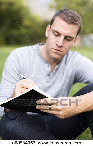 Portrait of young man writing journal in park View Large Photo Image Stock Photo - Portrait of young man writing journal in park. Fotosearch
