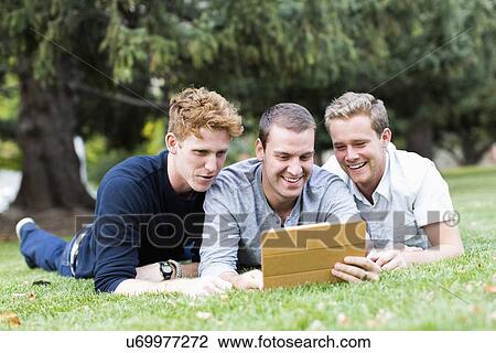 Stock Image - Portrait of young men using digital tablet in park. Fotosearch