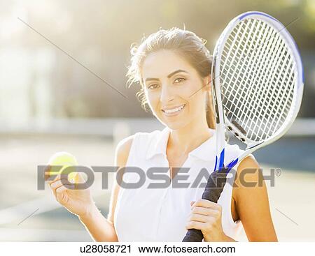 Stock Image - Portrait of young woman holding tennis ball and tennis racket. Fotosearch