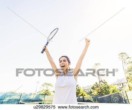 Portrait of young woman holding tennis racket, raising arms in celebration View Large Photo Image Stock Photography - Portrait of young woman holding tennis racket, raising arms in celebration. Fotosearch