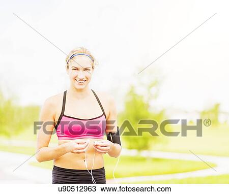 Stock Image - Portrait of young woman in sports clothing standing in park. Fotosearch