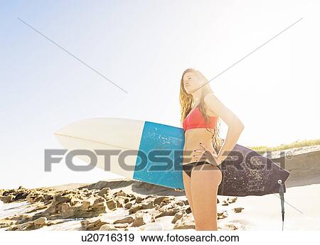 Portrait of young woman standing on beach, holding surfboard View Large Photo Image Stock Photo - Portrait of young woman standing on beach, holding surfboard. Fotosearch