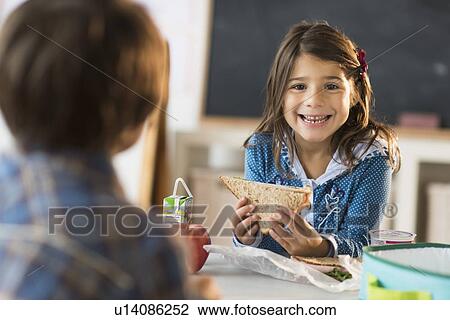 Stock Image - Pupils (6-7) eating lunch in classroom. Fotosearch