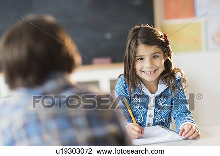 Stock Image - Pupils (6-7) learning in classroom, Girl (6-7) looking at camera. Fotosearch