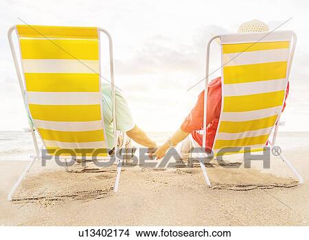 Rear view of couple sitting in lounge chairs on beach View Large Photo Image Picture - Rear view of couple sitting in lounge chairs on beach . Fotosearch
