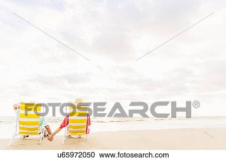 Rear view of couple sitting in lounge chairs on beach View Large Photo Image Stock Image - Rear view of couple sitting in lounge chairs on beach . Fotosearch