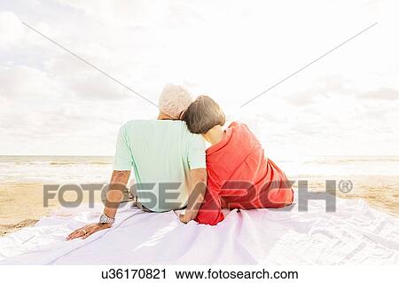 Rear view of couple sitting on beach at sunrise View Large Photo Image Stock Image - Rear view of couple sitting on beach at sunrise. Fotosearch