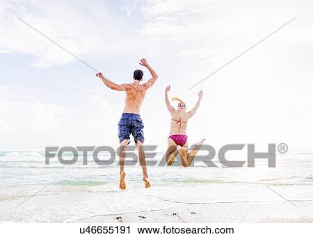 Rear view of young couple jumping on beach View Large Photo Image Stock Image - Rear view of young couple jumping on beach. Fotosearch