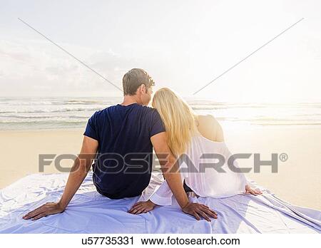 Rear view of young couple sitting on blanket on sandy beach, looking at sea View Large Photo Image Stock Image - Rear view of young couple sitting on blanket on sandy beach, looking at sea. Fotosearch