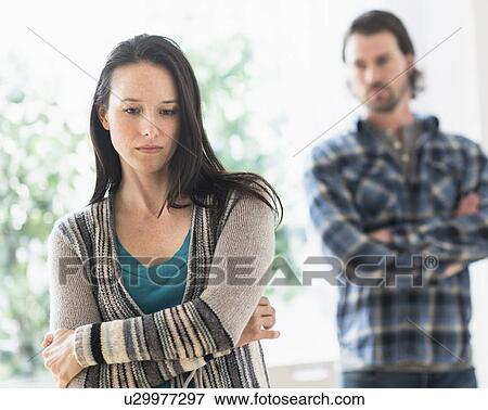 Stock Photo - Sad woman with arms crossed, man in background. Fotosearch