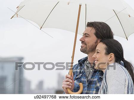 Stock Photo - Side view of couple under umbrella. Fotosearch