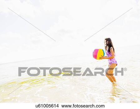Picture - Side view of girl (6-7) holding beach ball on beach. Fotosearch