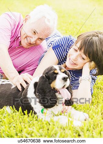 Stock Photo - Smiling couple with dog lying in grass. Fotosearch