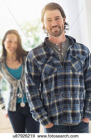 Stock Photo - Smiling man looking at camera, woman in background. Fotosearch