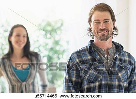 Stock Photography - Smiling man looking at camera, woman in background. Fotosearch