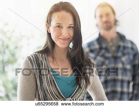 Stock Photo - Smiling woman looking at camera, man in background. Fotosearch